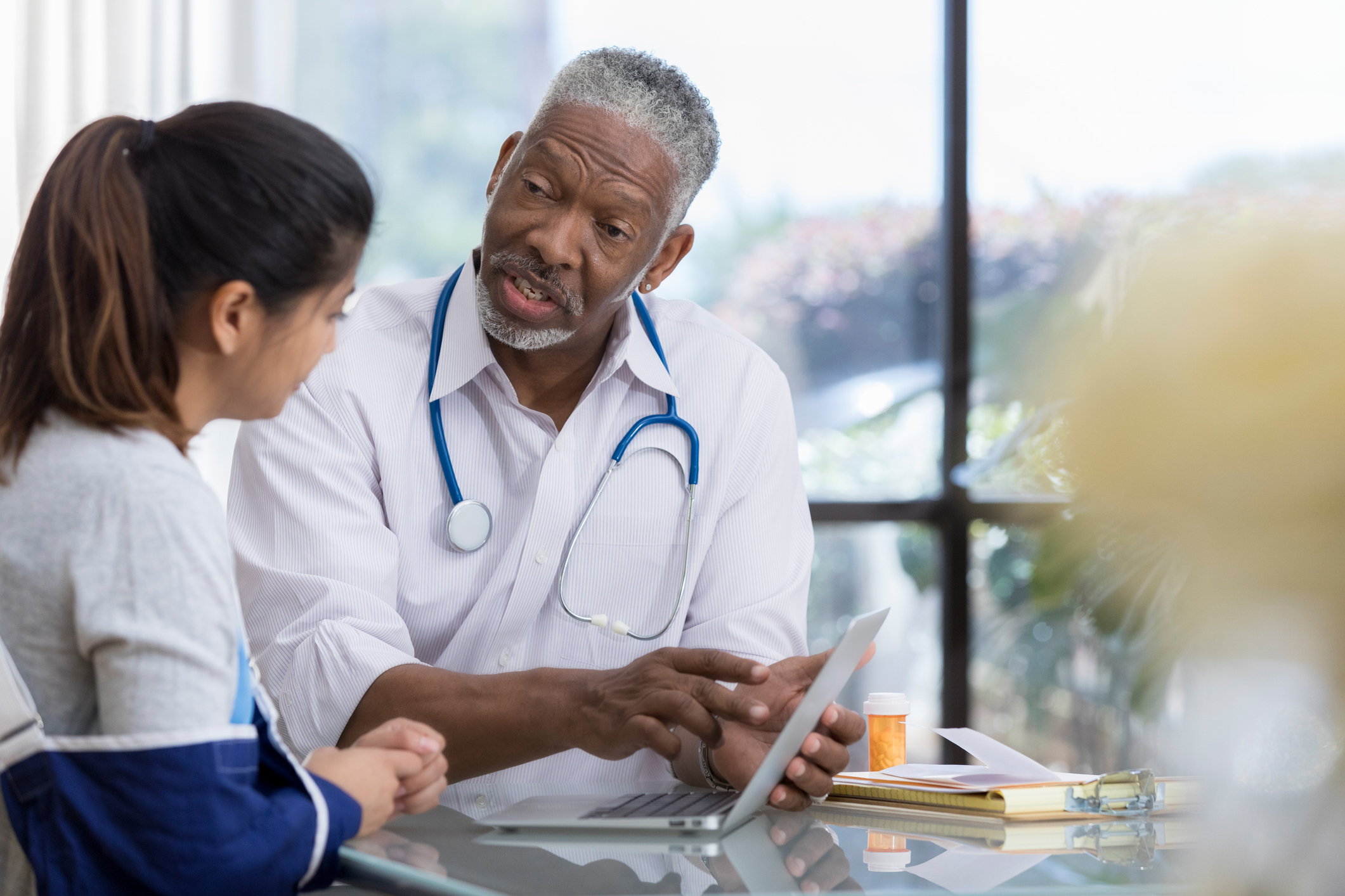 senior male doctor explains symptoms to patient using computer