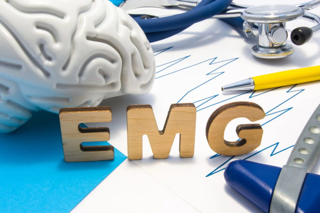 Wooden letters spelling EMG with wave data paperwork, pen, stethoscope, and brain model