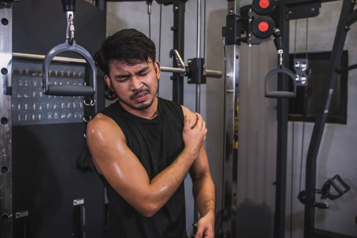 Young person experiencing shoulder pain while exercising in gym