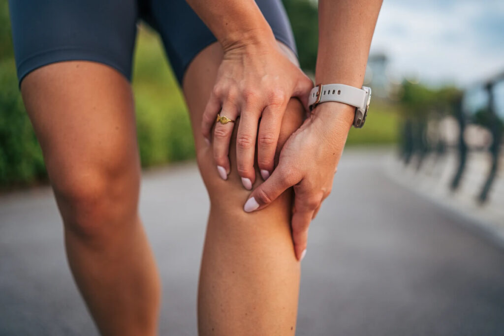 Young person holding front of knee in pain during outdoor run